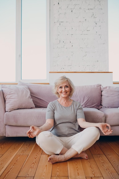 Femme âgée souriante pratiquant le yoga à la maison salon