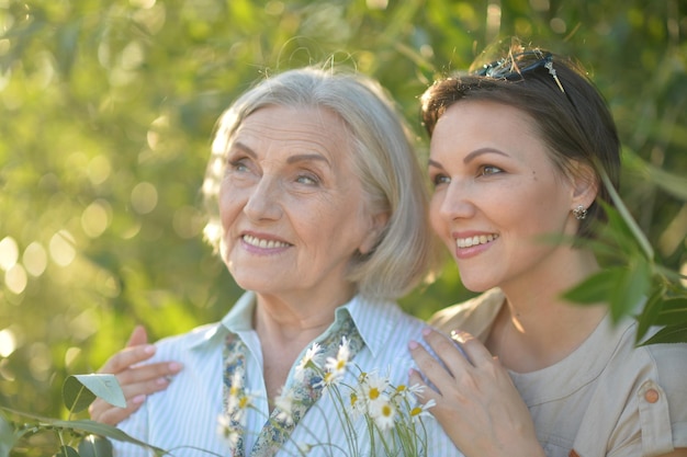 Femme âgée souriante avec sa fille adulte avec des fleurs dans le parc