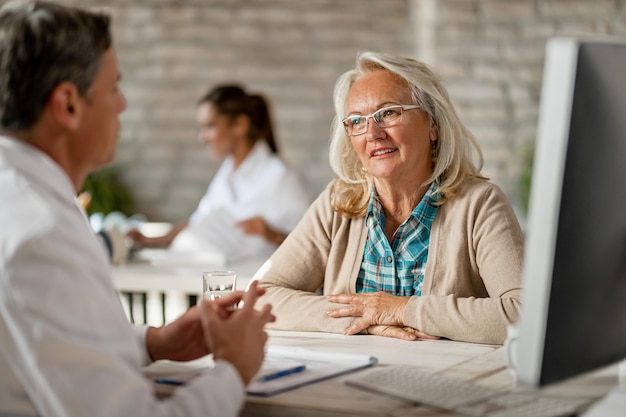 Une femme âgée souriante et son médecin discutent des options d'assurance médicale lors de consultations à la clinique