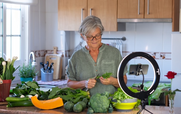 Une Femme âgée En Streaming En Ligne Suit Un Cours De Cuisine Végétarienne. Table De Cuisine à La Maison Pleine De Légumes Sains