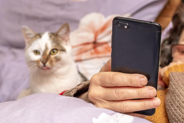 Une femme âgée avec un téléphone à la main près d'un chat au lit