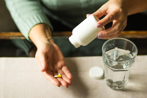 Une femme âgée tenant une bouteille de plastique blanche et deux capsules à la main prête à prendre des pilules supplémentaires