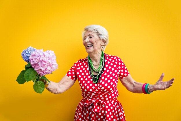 Une femme âgée tenant une fleur debout contre un fond coloré