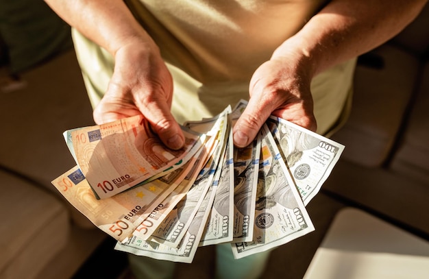 Une femme âgée tient dans ses mains de l'argent en dollars américains et en euros épargnés par le budget de planification de la retraite.
