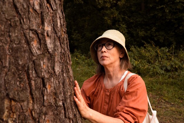 Une femme âgée touche un pin dans la forêt et parle avec un arbre