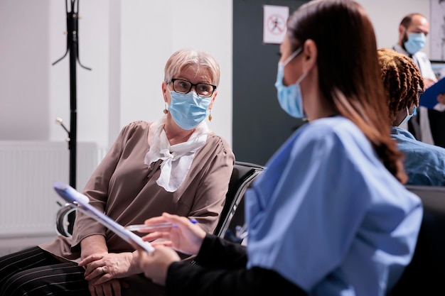 Femme âgée traitée par un médecin asiatique dans un sanatorium. Plan moyen d'un patient dans une clinique très fréquentée, consultation médicale. Femme médecin interviewant une patiente âgée dans la salle d'attente.