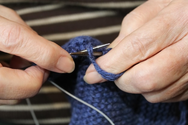 Une femme âgée tricote sur des aiguilles à tricoter avec des fils bleus.