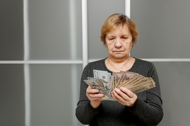 une femme âgée triste et concentrée qui compte des billets de banque dans ses mains