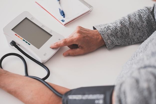 Femme âgée utilisant un appareil médical pour mesurer la pression artérielle femme âgée souffrant d'hypertension assise à la table de la maison en prenant soin de sa santé