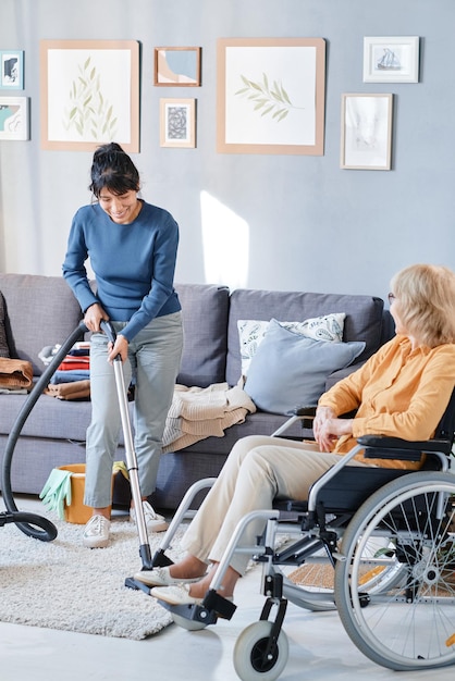 Photo femme âgée utilisant un fauteuil roulant parlant à une femme de ménage qui passe l'aspirateur sur le sol de la chambre