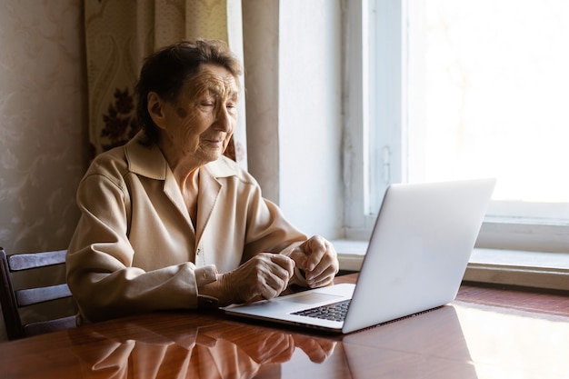 Une femme âgée utilise un ordinateur portable. Elle a l'air très surprise. Surfer dans un navigateur et les médias sociaux. Ordinateur portable sur la table. Utilisation de la technologie dans le concept de la vieillesse