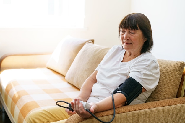 Femme âgée vérifiant le niveau de pression artérielle à la maison femme âgée souffrant d'hypertension artérielle ...