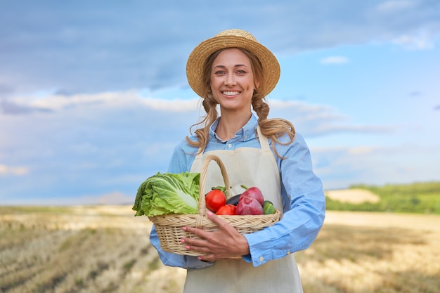 Femme agriculteur chapeau de paille tablier debout souriant des terres agricoles femme agronome spécialiste de l'agriculture agroalimentaire heureux positif caucasien travailleur champ agricole