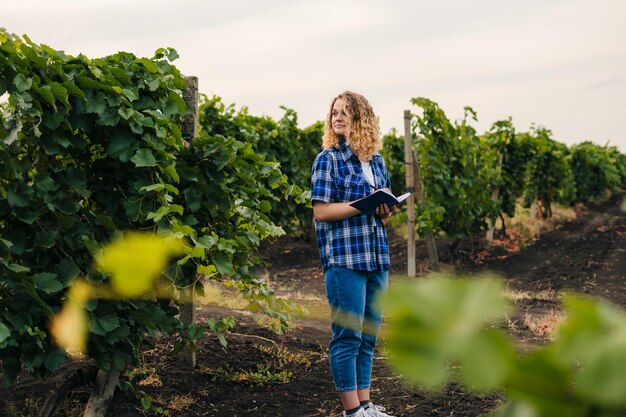 Femme agronome spécialiste debout au milieu des vignes vérifiant la qualité de la production de raisins Ferme avec une application mobile IOT et un concept d'agriculture intelligente