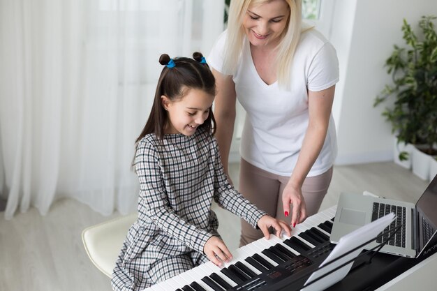 Femme aidant sa fille à jouer du piano, le corps et les boutons du piano ont été modifiés numériquement