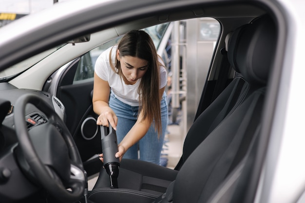 Femme à l'aide d'un aspirateur portable dans sa voiture Aspirateur électrique dans une voiture propre à la main de la femme à l'intérieur