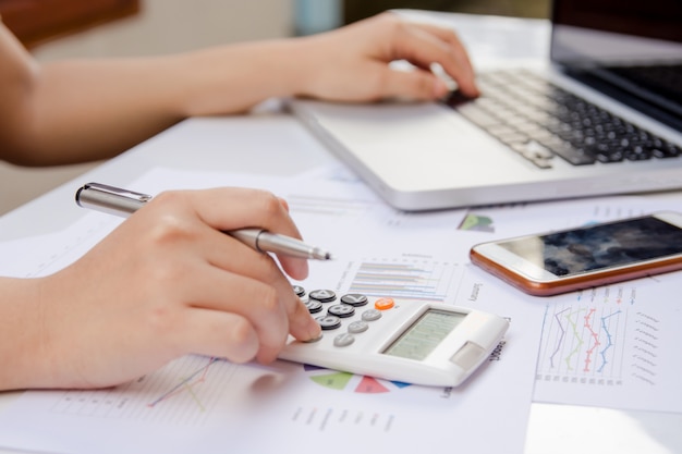 Femme à L'aide De La Calculatrice Et Ordinateur Portable Sur Les Données De Graphique Papier Avec Faire De La Finance Au Bureau.