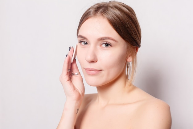 Femme à l'aide d'un coton. Heureuse belle jeune femme souriante nettoyant la peau avec un coton. fond clair. Belle Spa Femme Souriante. Peau fraîche parfaite. Concept de jeunesse et de soins de la peau