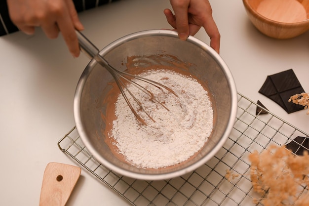 Femme à l'aide d'un fouet pour mélanger la farine à biscuits avec une pâte à biscuits au chocolat dans le bol à mélanger