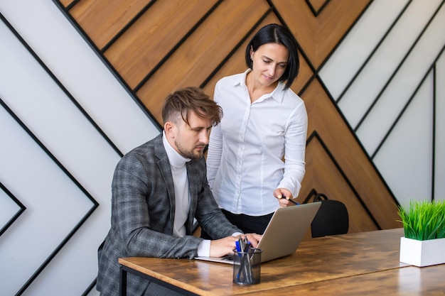 Une femme aide un homme à travailler sur un ordinateur portable au bureau