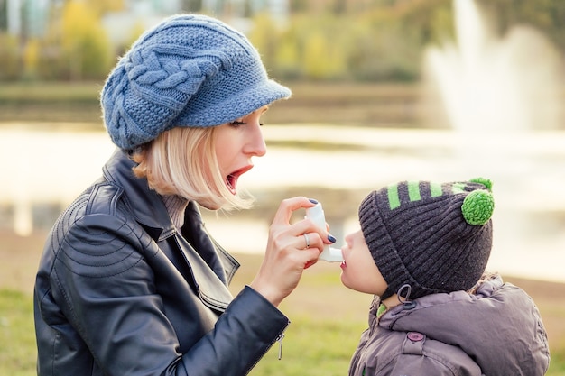 Femme à l'aide d'un inhalateur pour l'asthme à son fils dans un parc d'automne hiver froid