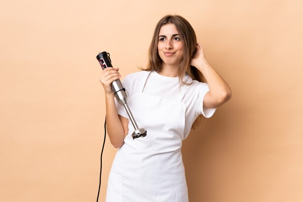 Femme à l'aide d'un mixeur plongeant sur un mur isolé ayant des doutes