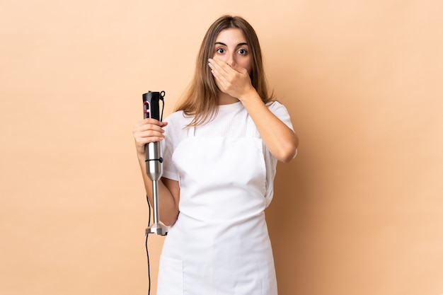 Femme à l'aide d'un mixeur plongeant sur un mur isolé couvrant la bouche avec les mains