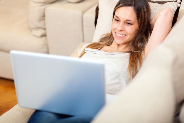 Femme à l'aide d'un ordinateur portable tout en vous relaxant sur le canapé