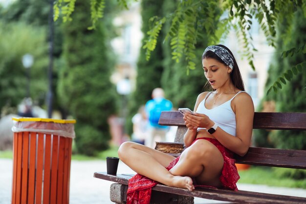 Femme à l'aide d'un smartphone dans le parc assis sur un banc