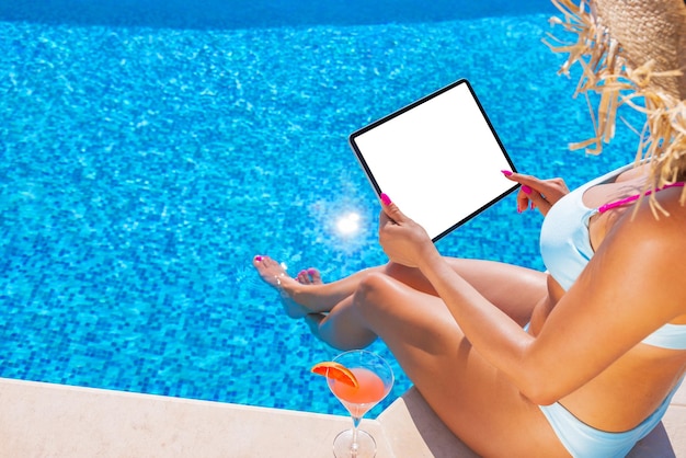 Femme à l'aide d'une tablette au bord de la maquette d'écran vierge de la piscine