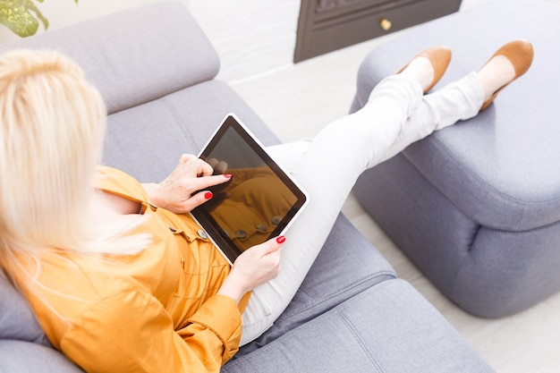 Femme à l'aide de tablette numérique sur canapé