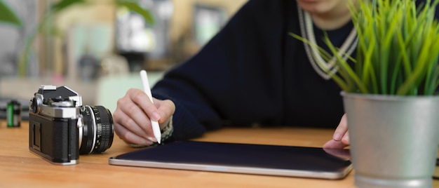 Femme à l'aide de tablette numérique sur table en bois avec appareil photo et pot d'arbre