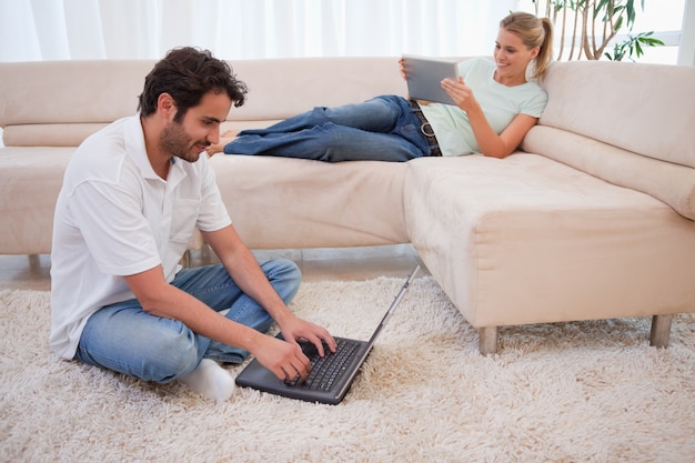 Femme à l&#39;aide d&#39;une tablette pendant que son mari utilise un ordinateur portable