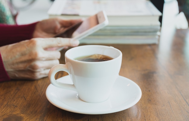 Femme à l&#39;aide d&#39;une tablette avec une tasse de thé sur une table en bois.