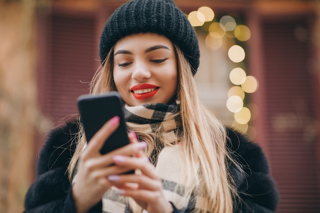 Femme à l'aide de téléphone portable par temps froid à l'extérieur dans les rues urbaines