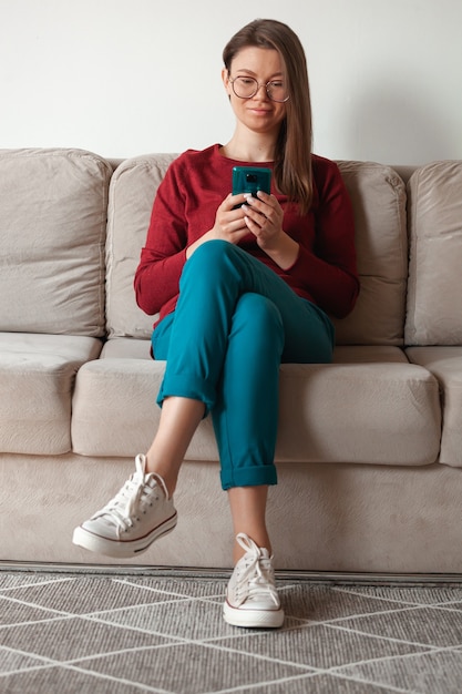 Femme à l'aide de téléphone portable, tenant dans les mains assis sur un canapé