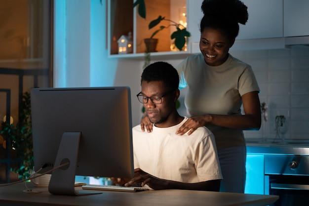 Une femme aimante soutient son mari, un concepteur de sites Web indépendant, travaillant sur un projet de petite entreprise à la maison tard