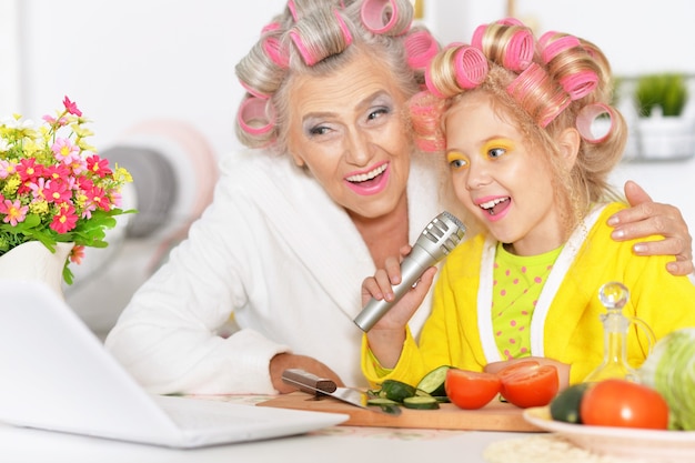 Femme aînée et petite-fille à la cuisine avec des légumes et un ordinateur portable