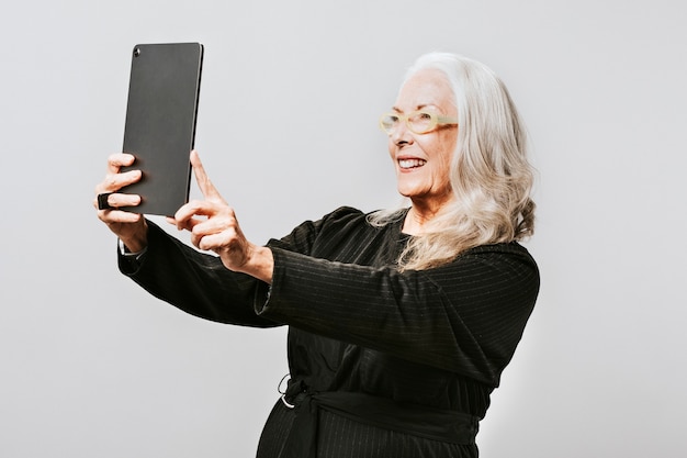 Femme aînée prenant une photo d'elle-même avec une tablette numérique