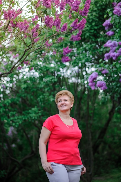 Femme aînée en tenue décontractée posant près d'un lilas en fleurs.