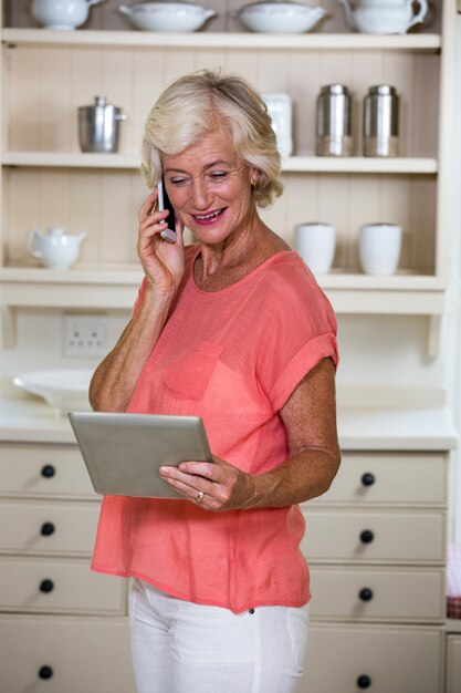 Femme aînée, utilisation, tablette numérique, et, téléphone portable, dans, cuisine