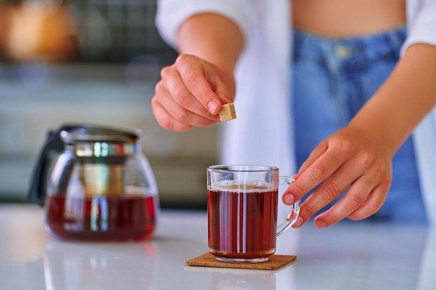 Femme ajoutant du cube de sucre brun de canne au thé noir dans la cuisine à domicile