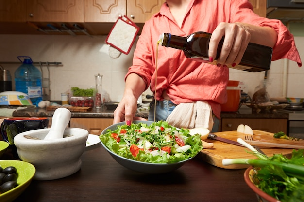 Femme ajoutant de l&#39;huile d&#39;olive dans une salade grecque saine