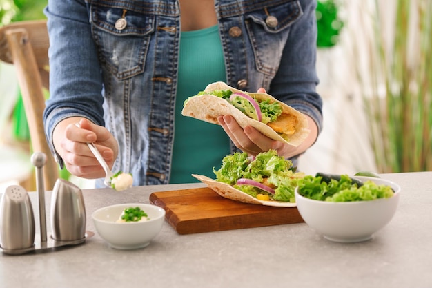 Femme ajoutant de la sauce à un délicieux taco de poisson dans la cuisine