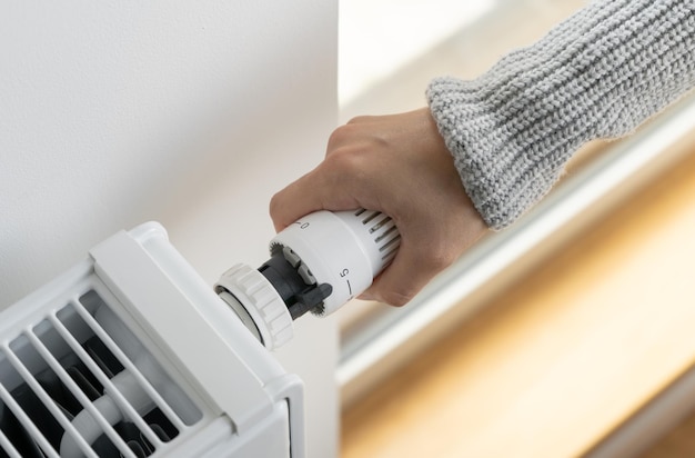 Une femme ajuste le thermostat du radiateur à la température maximale de la pièce