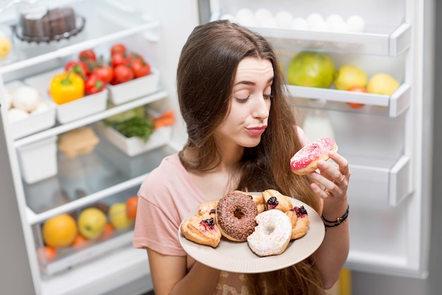 Femme avec des aliments sucrés près du réfrigérateur