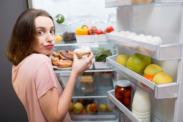 Femme avec des aliments sucrés près du réfrigérateur