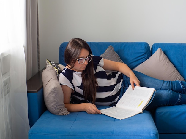 Femme allongée sur un canapé bleu dans le salon et lisant les nouvelles