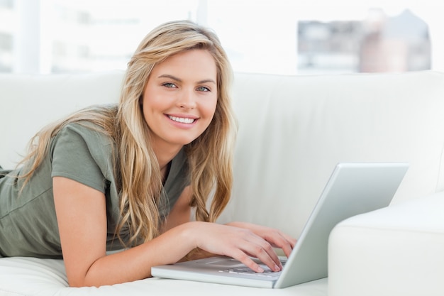 Femme allongée sur le canapé avec un ordinateur portable en face d&#39;elle, souriant