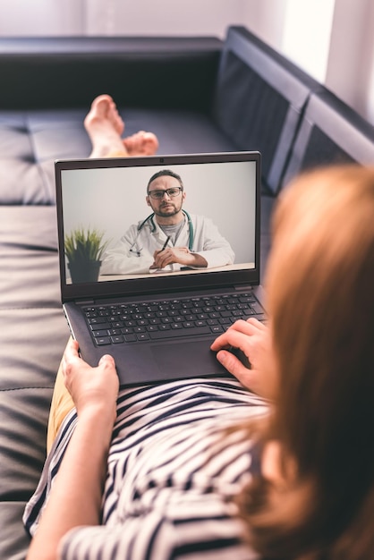 Femme allongée sur un canapé et parler avec un médecin en ligne à l'aide d'un ordinateur portable Concept de télémédecine